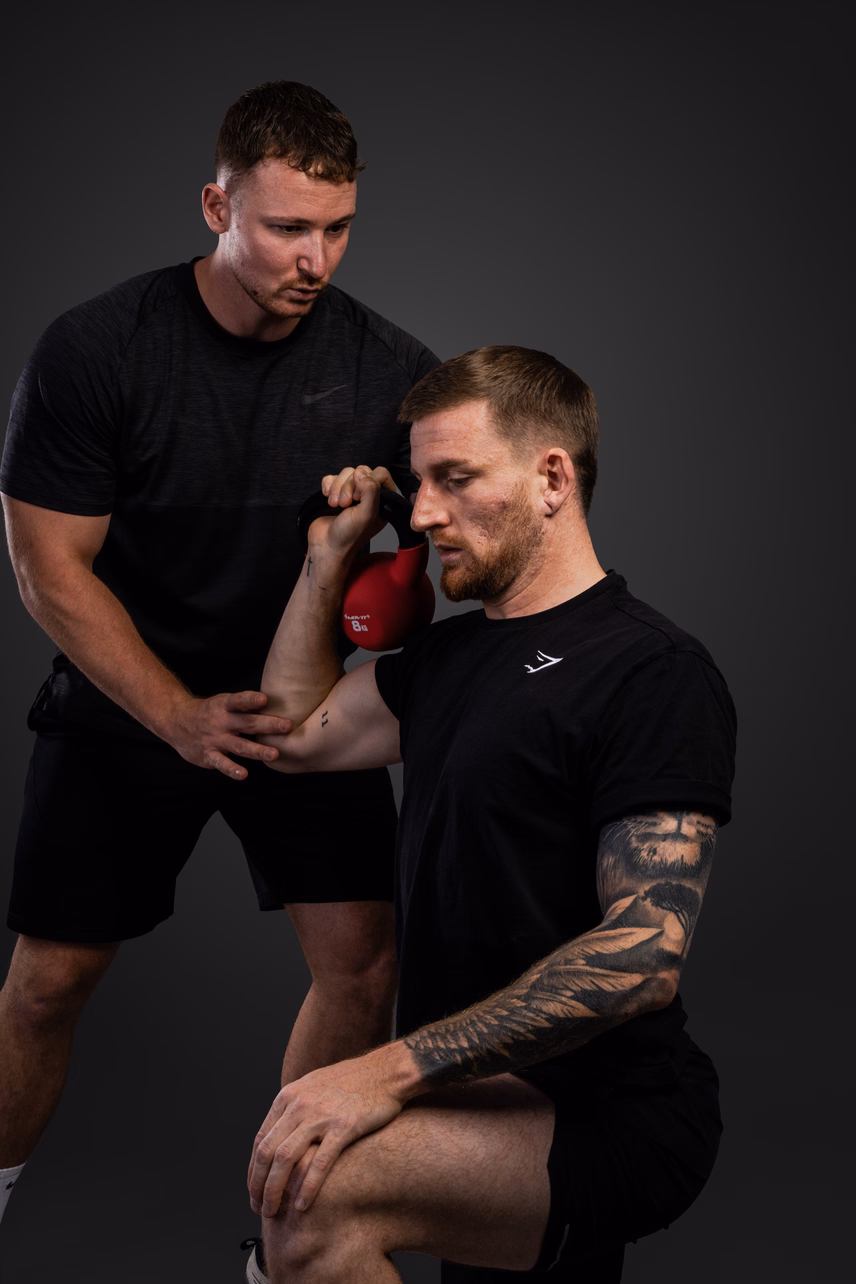 Zwei Männer beim Training mit einer Kettlebell. Einer gibt Anleitung und Unterstützung.