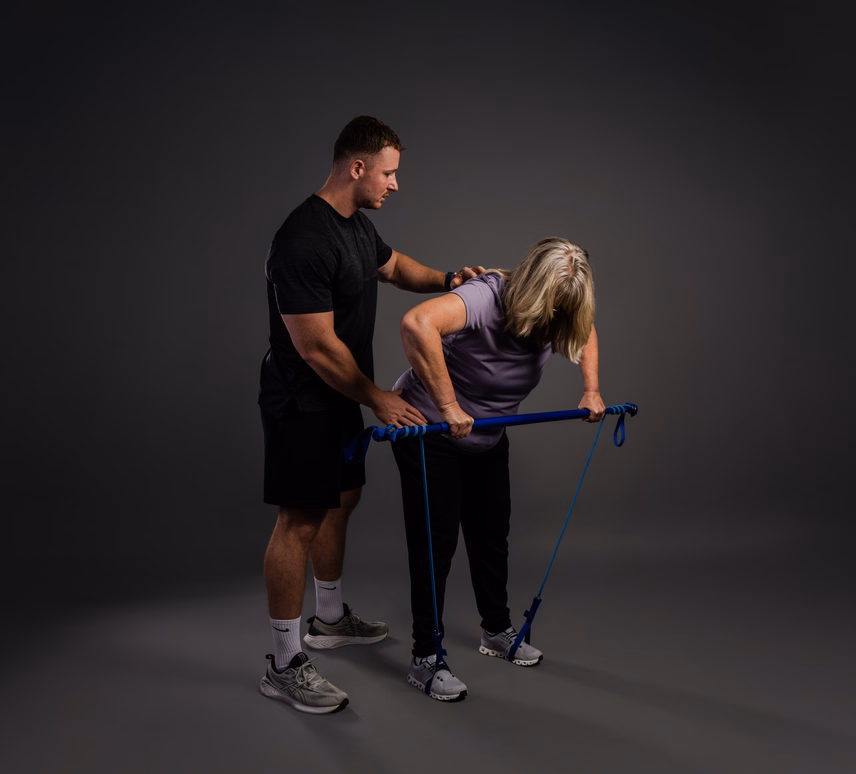 Eine Person trainiert mit einem Fitnessband unter Anleitung eines Trainers.